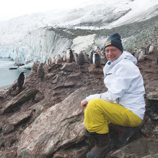 Dr. Peter Hartig während seiner wissenschaftlichen Expedition in der Antarktis, umgeben von Pinguinen vor einer Eiskulisse.